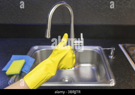 Großartiges Konzept für die Hausreinigung, Hand mit Handschuh macht positive Zeichen mit Daumen Stockfoto