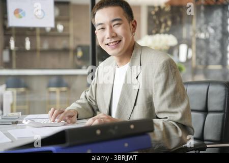 Lächelnder junger asiatischer Geschäftsmann im modernen Büro. Gutaussehender asiatischer Mann glücklich und freundlich während der Arbeit Erfolg Job Stockfoto