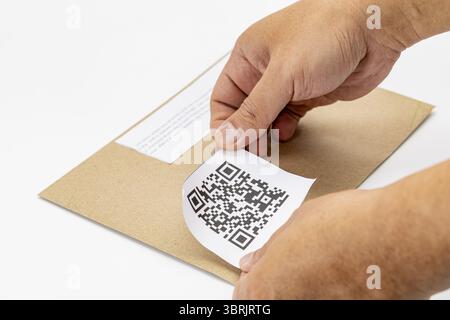 Eine Person klebt ein qr-Code-Etikett auf einem braunen Umschlag und demonstriert damit eine moderne und effiziente Art und Weise, Informationen zu verwalten. Das Etikett vorsichtig mit den Händen anbringen Stockfoto