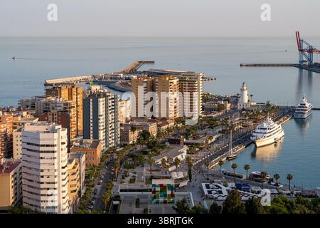 Stadt von oben gesehen. Ikonischer Leuchtturm und pulsierende Küste von Málaga bei Sonnenuntergang, Luxusyachten, palmengesäumte Boulevards und urbanes Leben am Meer. Stockfoto