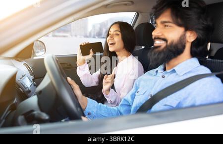 Indianerin singt mit Smartphone, während ihr Freund Auto fährt Stockfoto