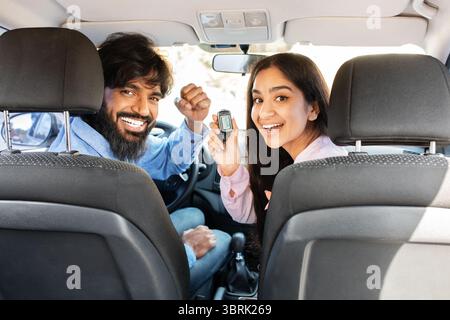 Fröhliches indisches Paar zeigt Autoschlüssel zur Kamera und feiert den Besitzer eines neuen Autos Stockfoto
