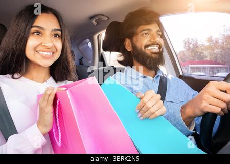 Glückliches Indianerpaar im Auto nach dem Einkaufen, mit bunten Taschen vor Freude Stockfoto