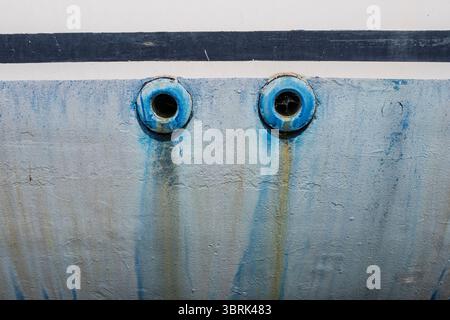 Detail zweier blauer kreisförmiger Bootsabflüsse mit Rost- und Wasserstreifen auf einer abgenutzten Rumpfoberfläche Stockfoto