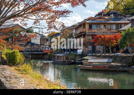 Arashiyama, Kyoto, Japan. Traditionelle Yakatabune-Vergnügungsboote aus Holz liegen im Herbst auf dem Oigawa River vor klassischen japanischen Gasthäusern. Stockfoto