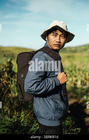 Nahaufnahme eines südostasiatischen jungen Mannes in einem Eimerhut und einer blauen Jacke mit schwarzem Rucksack, während er das üppige grüne Tal bei M erforscht Stockfoto