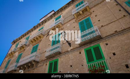 Blick nach oben auf das traditionelle italienische Gebäude mit grünen Fensterläden und weißen Balkonen in Tropea, Kalabrien, unter blauem Himmel Stockfoto