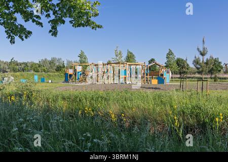 Lebendiger, moderner Spielplatz inmitten von üppigem grünem Gras und Bäumen unter einem klaren blauen Himmel, perfekt für Themen wie Kindheit, Erholung und Outdoor-Spaß Stockfoto