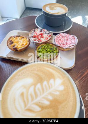 Latte Art Kaffeetasse vor verschiedenen Gebäckstücken auf einem Teller, mit lebhaften Torten, die eine warme und einladende Café-Szene für Dessertfans schaffen Stockfoto