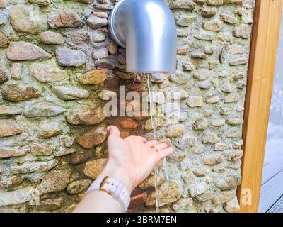 Ein Mädchen fängt Wasser aus einer Mineralquelle auf einem Berg in Harrachov, Tschechien. Hochwertige Fotos Stockfoto