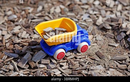 Ein hellblauer Spielzeugkipper mit roten Rädern und einem gelben Kippbett mit Holzspänen sitzt auf einer Mulchfläche und schafft so eine verspielte Co Stockfoto