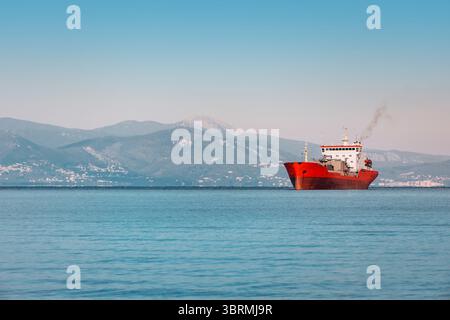 Frachtschiff segelt auf ruhigem Meer bei Sonnenuntergang mit Bergen im Hintergrund, Seeverkehrskonzept Stockfoto