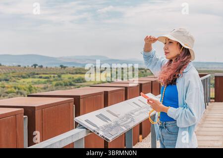 5. Mai 2025, Canakkale, Türkei: Junge Frau, die Augen mit der Hand abschirmt, während sie eine Informationstafel über die Landschaft an einem Aussichtspunkt liest Stockfoto