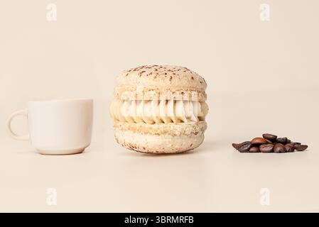 Latte Macaron mit Kaffeetasse und gerösteten Bohnen auf beigefarbenem Hintergrund Stockfoto
