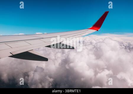 Flugzeugflügel, der durch den blauen Himmel schwingt, flauschige weiße Wolkenlandschaft darunter, die einen malerischen Blick aus der Luft bietet Stockfoto