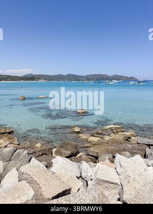 Ruhige Küstenszene mit klarem blauem Wasser, sichtbaren Felsen und weit entfernten Booten unter klarem Himmel. Die ruhige Umgebung lädt zum Entspannen ein Stockfoto