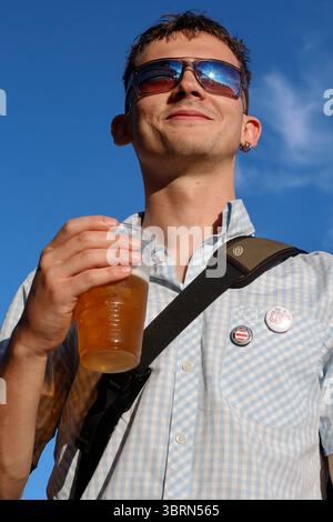 Ein junger Mann trinkt ein Pint Lager aus einem Plastikbecher Stockfoto