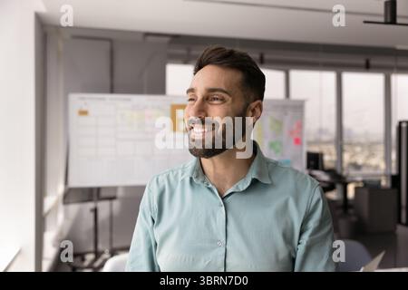 Geschäftsmann steht im Büro, blickt mit einem zufriedenen Lächeln aus dem Fenster Stockfoto