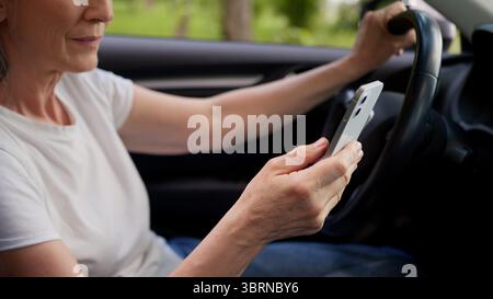 Nahaufnahme unbekannte kaukasische ältere Frau Frau reifer Seniorenpensionär Autobesitzer in einem Elektroauto, die Nachricht mit dem Handy schreiben Stockfoto