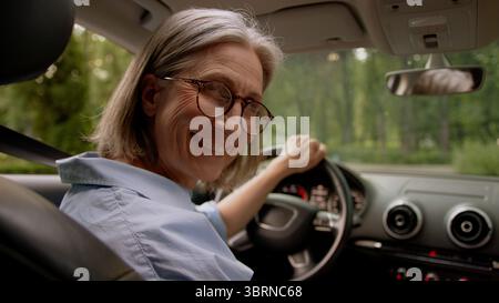 Rückansicht glücklich lächelnd kaukasisch alt ältere Frau fröhlich reife ältere Frau Taxifahrerin, die im Auto fährt und das Lenkrad fährt Stockfoto