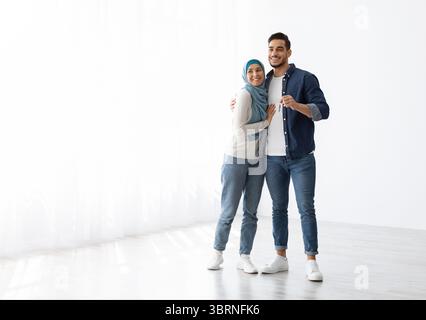 Glückliches muslimisches Paar posiert in leerer Wohnung und zeigt den Schlüssel Stockfoto