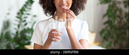 Fröhliche junge afroamerikanische Frau nimmt eine Pille Vitamine Und Getränke mit einem Glas Wasser Stockfoto