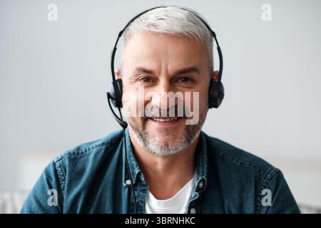 Lächelnder älterer Mann, der eine Videokonferenz mit einem Headset führt Stockfoto