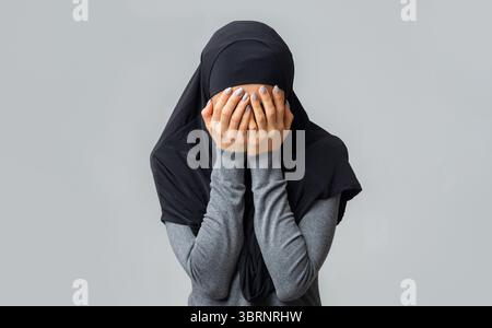Muslimische Frau in schwarzem Hijab, die das Gesicht mit Händen bedeckt Stockfoto