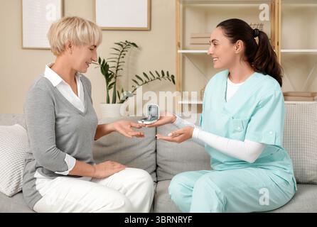 Arzt gibt reiferen Frauen Hörhilfe, während sie zu Hause besuchen Stockfoto