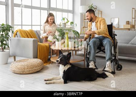 Junger Mann im Rollstuhl, mit Frau und Zimmerpflanzen zu Hause Stockfoto