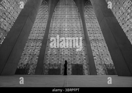 Eine Frau in traditioneller Kleidung steht in einem riesigen, reich verzierten Saal mit komplexen geometrischen Mustern an hoch aufragenden Wänden und Schwarz-weiß-Innenaufnahmen Stockfoto