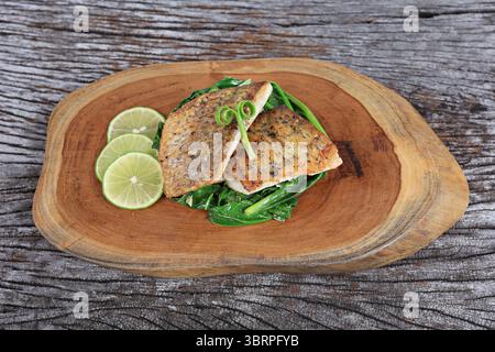 Seebarschsteak serviert mit Salat in Olivenöl und Zitronenscheiben auf Holztablett Stockfoto