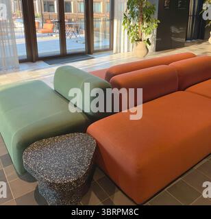 Loungebereich in der Fensternähe mit Vorhängen. Sofa in sanftem Orange und Grün. Moderne Möbel. Design im Innenraum. Stockfoto