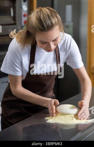 Die Bäckerin konzentriert sich beim Kneten von Teig auf der Arbeitsplatte Stockfoto