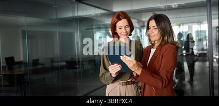 Zwei beschäftigte, glückliche Geschäftsfrauen, die sich mit TAB unterhalten und im Büro arbeiten. Stockfoto