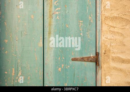 Alte türkisfarbene Holztür mit rustikalen Scharnieren, Holztür in Steinmauer Stockfoto
