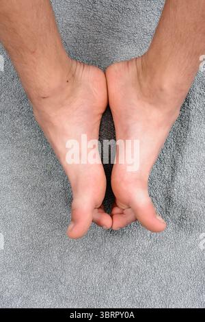 Ein Top-Down-Schuss von einem Paar Füße, Sohlen hoch, auf einem weichen, grauen, strukturierten Handtuch. Das Bild vermittelt ein Gefühl der Entspannung und des Komforts. Stockfoto