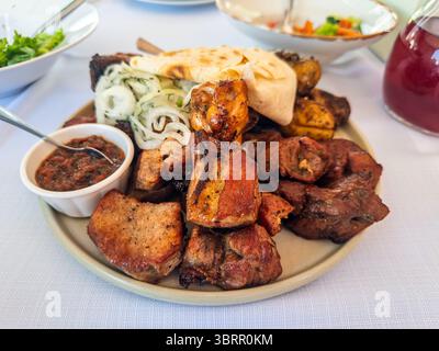 Eine großzügige Platte mit gemischtem gegrilltem Fleisch, einschließlich Schweineschaschlik und Huhn, serviert mit rustikalen Röstkartoffeln und frischem Lavaschbrot auf einem Stockfoto