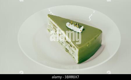 Ein Stück grüner Matcha-Kuchen, gekrönt mit einem kleinen Klecks Sahne und garniert mit zerstoßenen Pistazien, ein Stück viraler Dubai-Schokoladenkuchen auf einem Whei Stockfoto