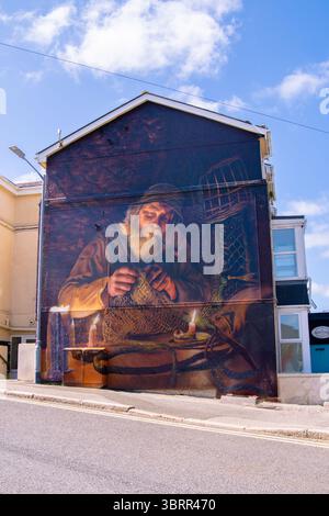 Lebendiges Wandbild eines traditionellen kornischen Fischers, der Netze bei Kerzenlicht repariert, gemalt an der Seite eines Gebäudes in Newquay, Cornwall, Großbritannien. Stockfoto
