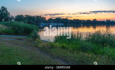 Segelschiffe im Hafen von Hard am Bodensee vor Sonnenaufgang beleuchtet die Dämmerung den See und zaubert intensive Farben auf das Wasser Stockfoto