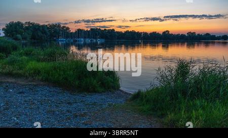Segelschiffe im Hafen von Hard am Bodensee vor Sonnenaufgang beleuchtet die Dämmerung den See und zaubert intensive Farben auf das Wasser Stockfoto