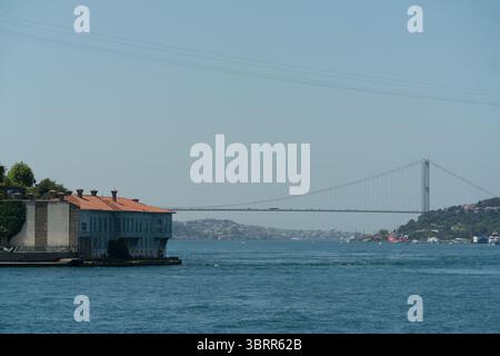 Historische Gebäude säumen den Bosporus mit einer modernen Brücke, die in der Ferne sichtbar ist und Istanbuls architektonischen Kontrast an einem sonnigen Tag zeigt. Stockfoto
