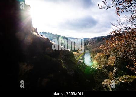 Ein dramatischer, sonnenverwöhnter Weitwinkelblick auf einen sich windenden Fluss in einem tiefen Tal, umgeben von Herbstbäumen, mit auffälligen Sonnenlichtern. Stockfoto