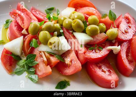 Frisch geschnittene Tomaten mit Olivenöl, garniert mit grünen Oliven, Zwiebeln, Knoblauch und Basilikum, zu einem einfachen, aber geschmackvollen Salat Stockfoto