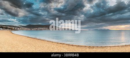 Faszinierender Panoramablick auf einen mediterranen Strand in Dikili, Turkiye, mit einem dramatischen Himmel voller lebendiger Farben während eines atemberaubenden Sonnenuntergangs Stockfoto