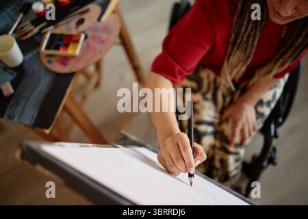 Frau mit Behinderung zeichnet auf Leinwand im Rollstuhl Stockfoto