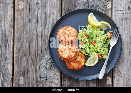 Geräucherte Lachsburger, Pasteten oder Kuchen serviert mit Krautsalat und Zitronenscheiben auf einem Teller mit Gabel auf rustikalem Holztisch, Blick von oben, flacher Lay, kostenloses Spa Stockfoto