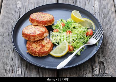 Geräucherte Lachsburger, Pasteten oder Kuchen serviert mit Krautsalat und Zitronenscheiben auf einem Teller mit Gabel auf rustikalem Holztisch, Nahaufnahme, nicht KI generiert Stockfoto