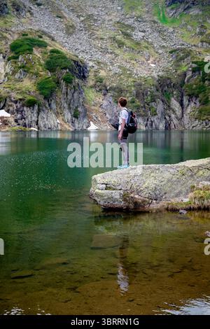 Mann, der auf Felsen am Alpensee in den österreichischen Bergen steht Stockfoto